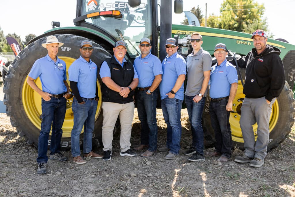 A crew of Ascenso workers smiling in front of a John Deere tractor.