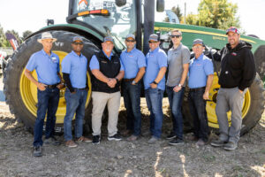 A crew of Ascenso workers smiling in front of a John Deere tractor.