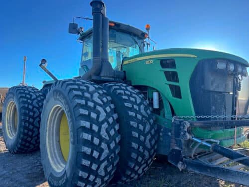 John Deere tractor with MDR 1000 tires against a blue sky in a dirt field. 